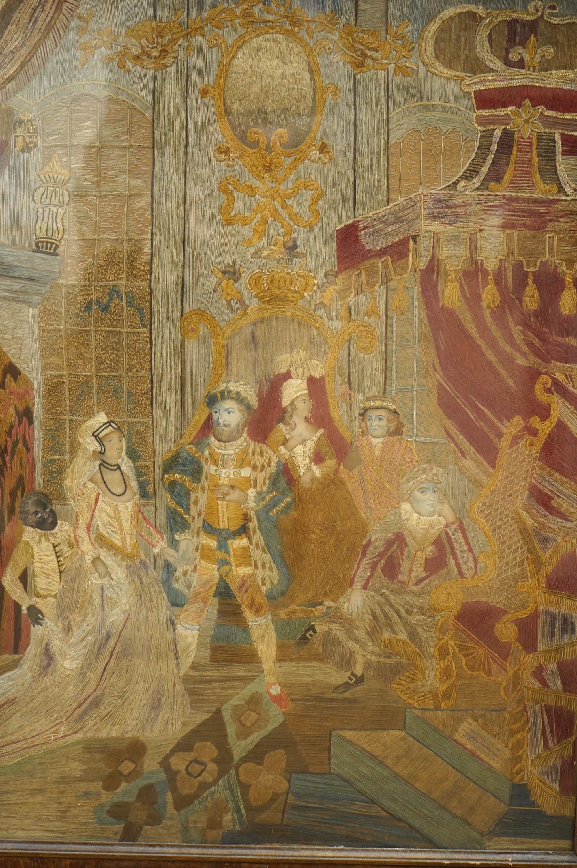 A large unusual Regency framed silk worked embroidery depicting Henry VIII in court with three courtiers and a blackamoor servant holding the dress of a young female courtier as she enters, worked mainly in long stem sti